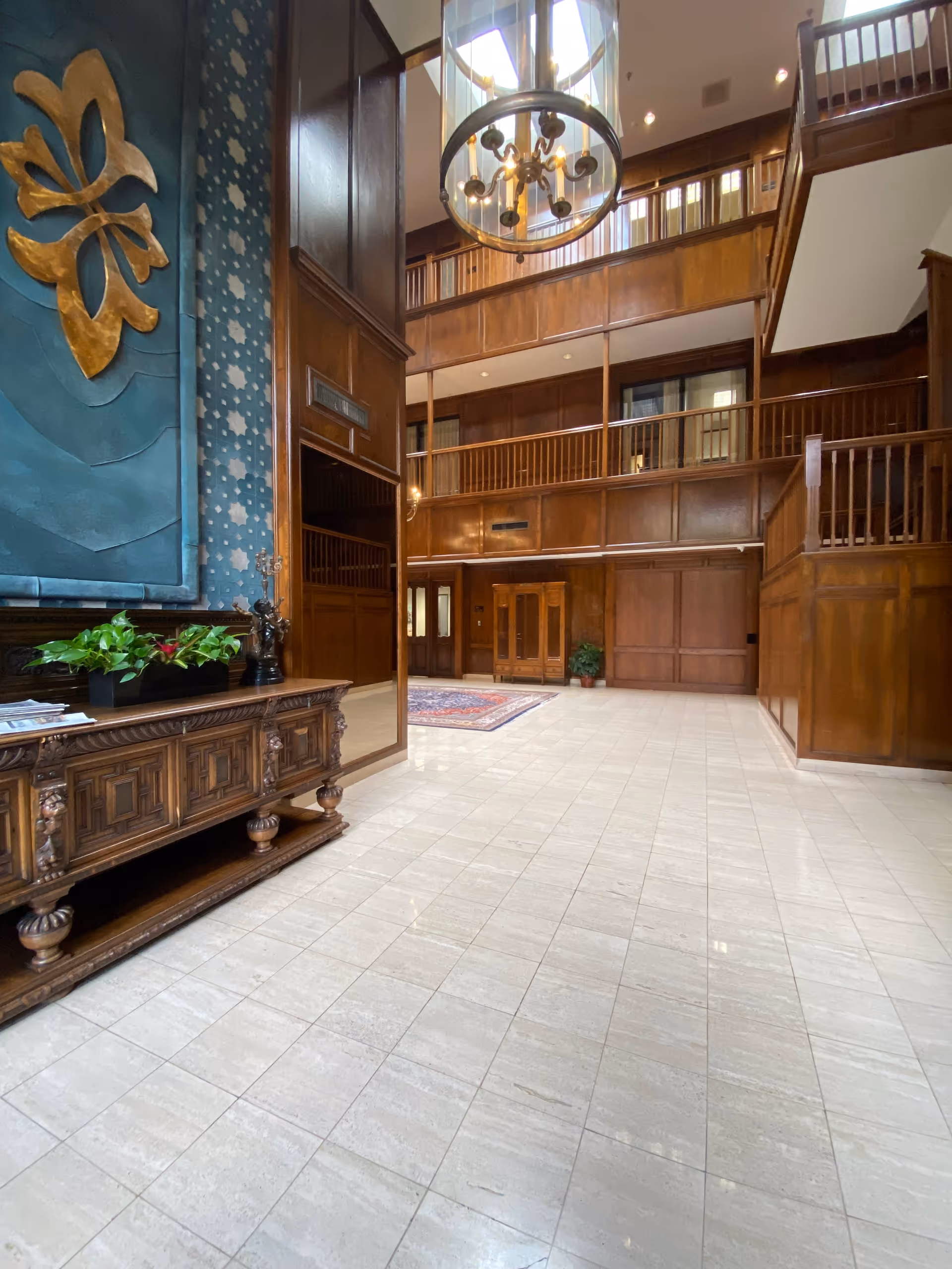 Wood-paneled lobby with staircase and chandelier in a senior living facility.