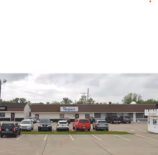 Front view of a single-story strip mall with a Helpers sign and parked cars.