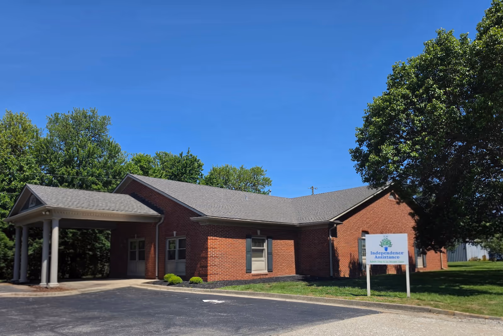 Red brick senior living facility with covered entrance and Independence Assistance sign.