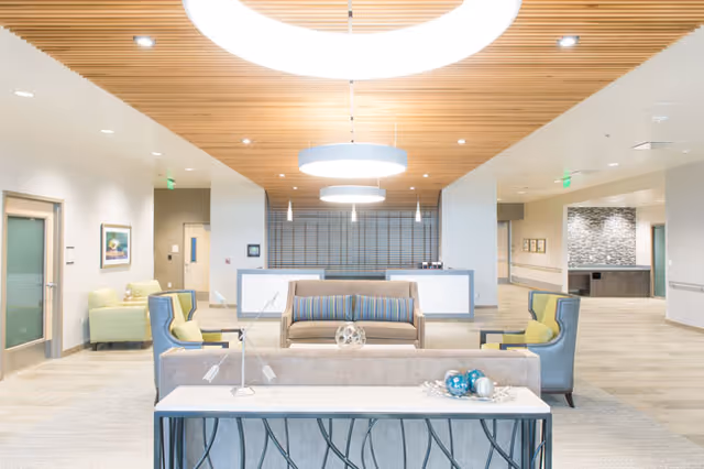 Bright, modern senior living lounge with sofas, a reception desk, and circular pendant lights.