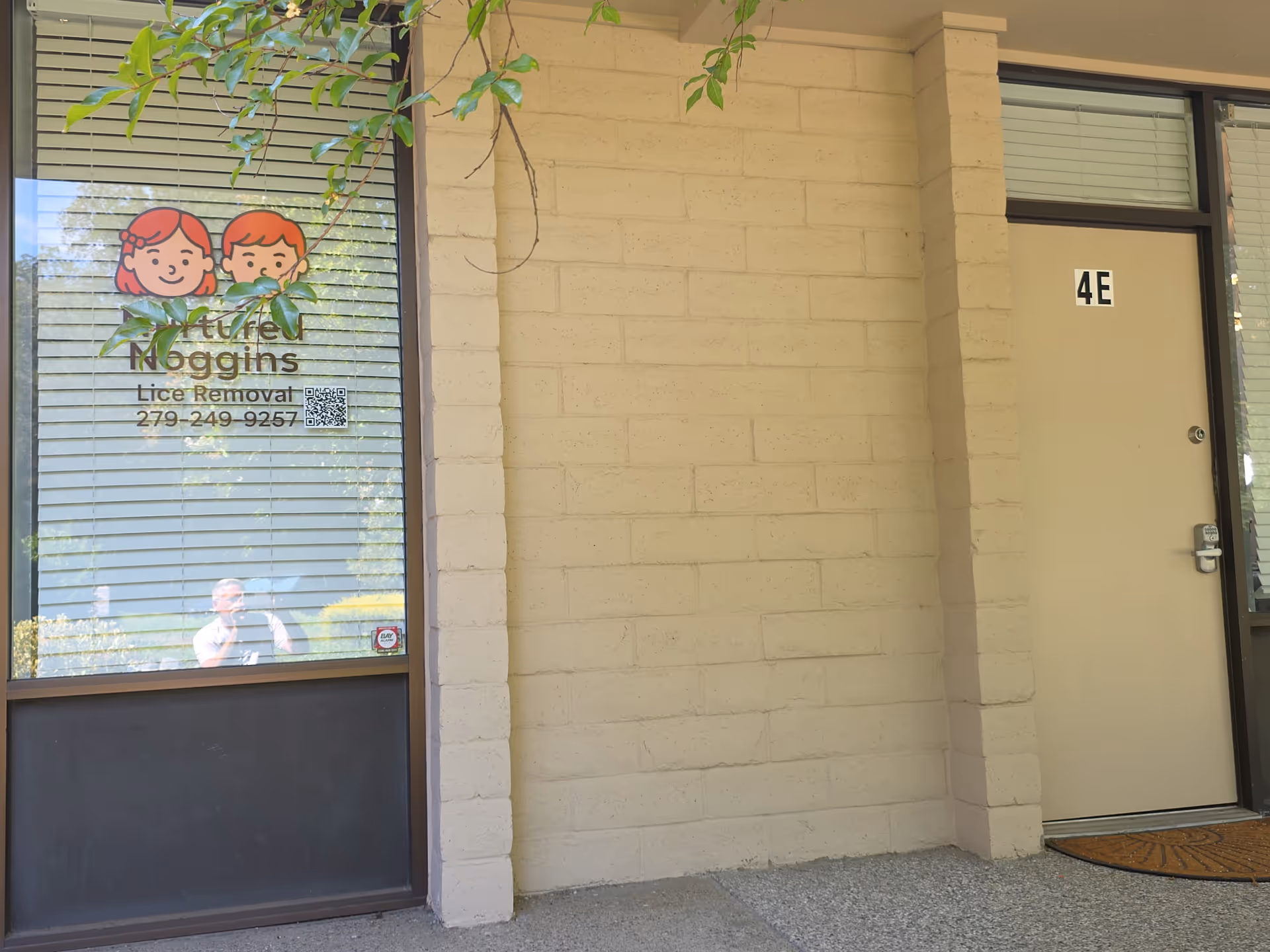 Exterior view of a beige brick building with 4E door and window advertising Nurtured Noggins.