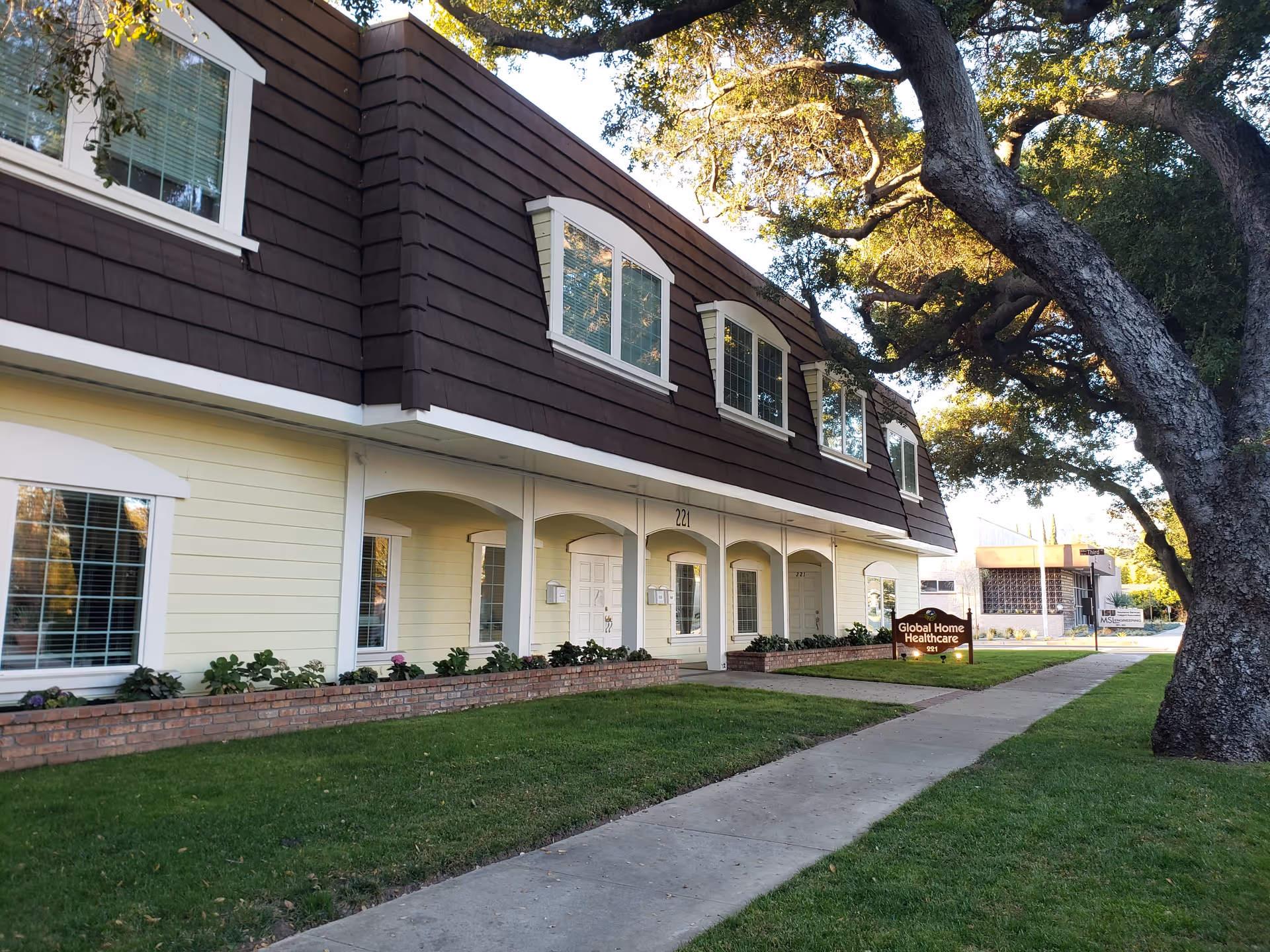 Exterior view of a two-story senior care building with a manicured lawn, sidewalk, and main entrance.