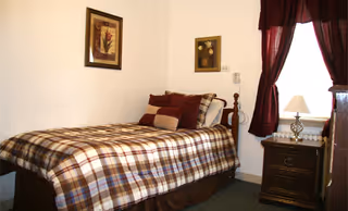 A cozy bedroom with a plaid bedspread, framed art, and burgundy curtains.
