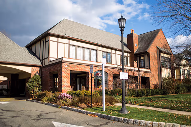 Exterior view of a brick senior living facility with Tudor-style architecture and a streetlamp.