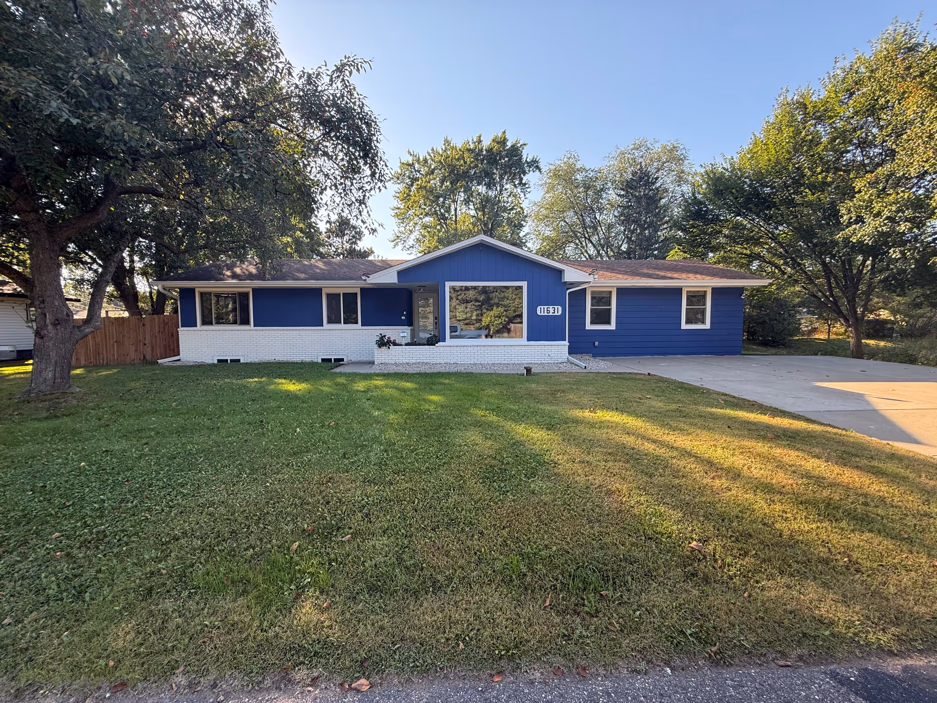 Blue single-story house with white brick foundation, front yard, and driveway.