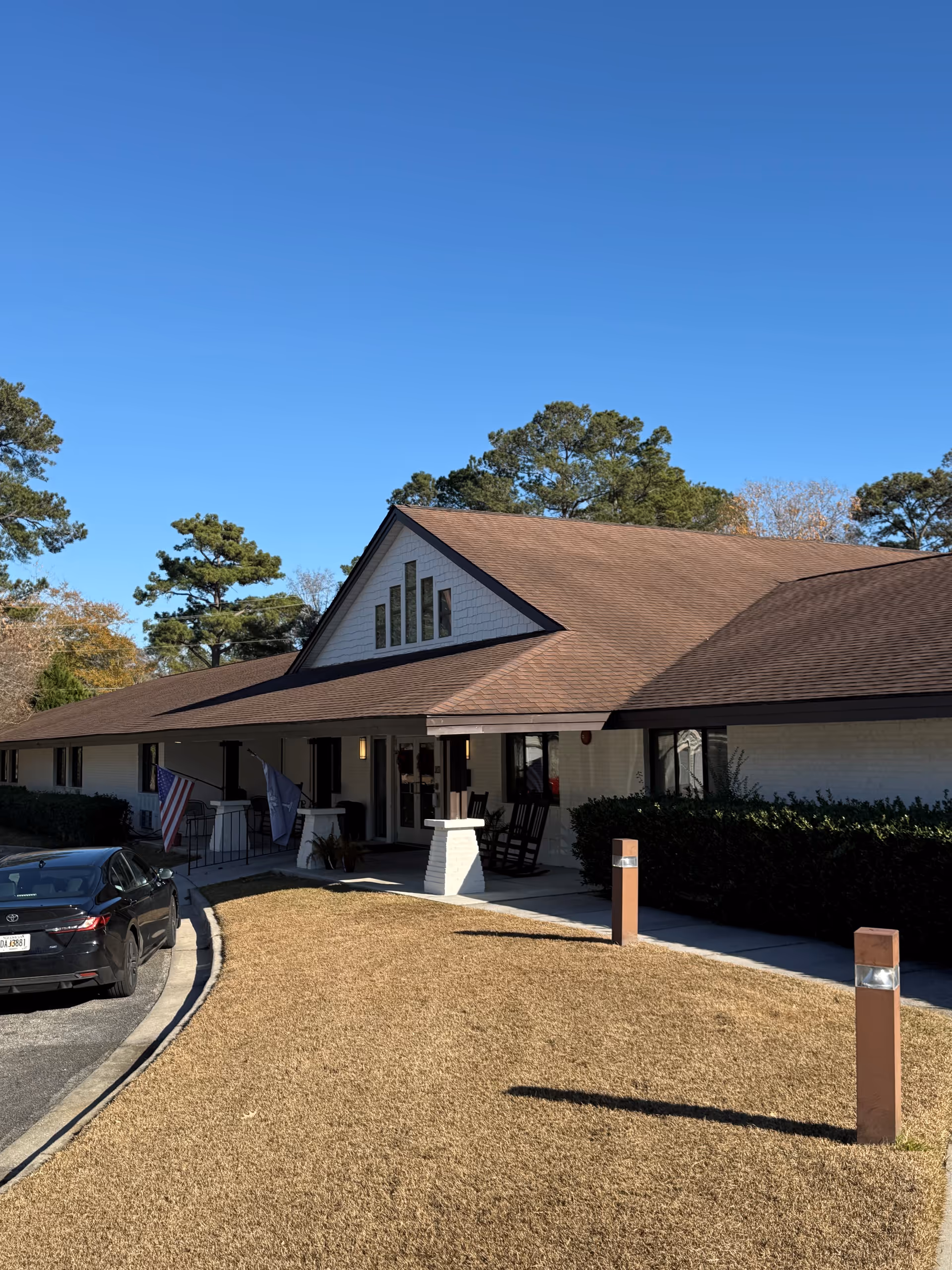 Low, long building with brown roof and front entrance, cars parked outside under a clear sky.