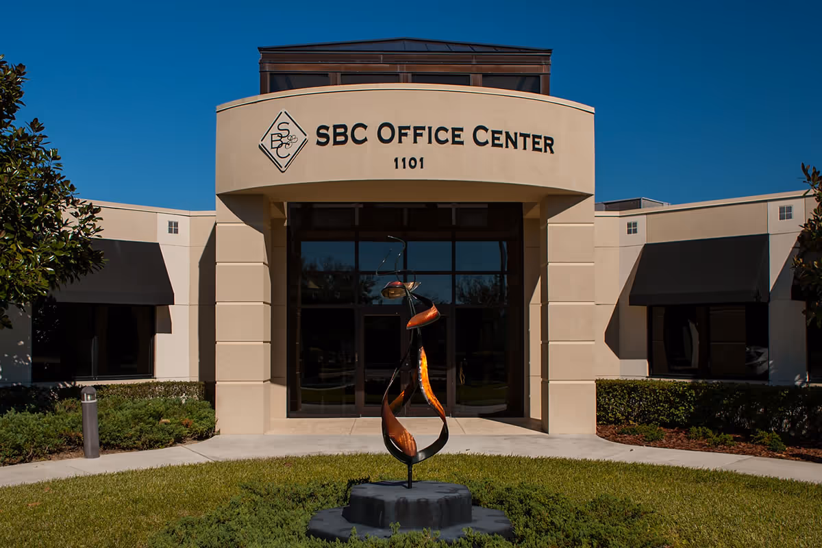 Front exterior of a beige office building with a curved entrance and sculpture.