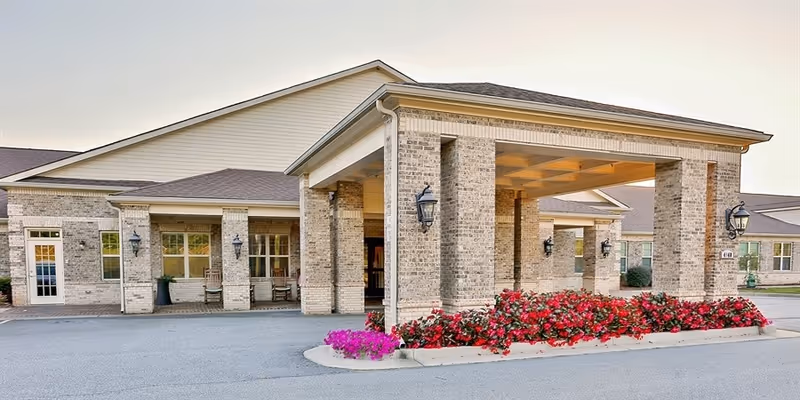 Country Square senior living facility exterior with brick pillars, covered entrance, and colorful flower beds.