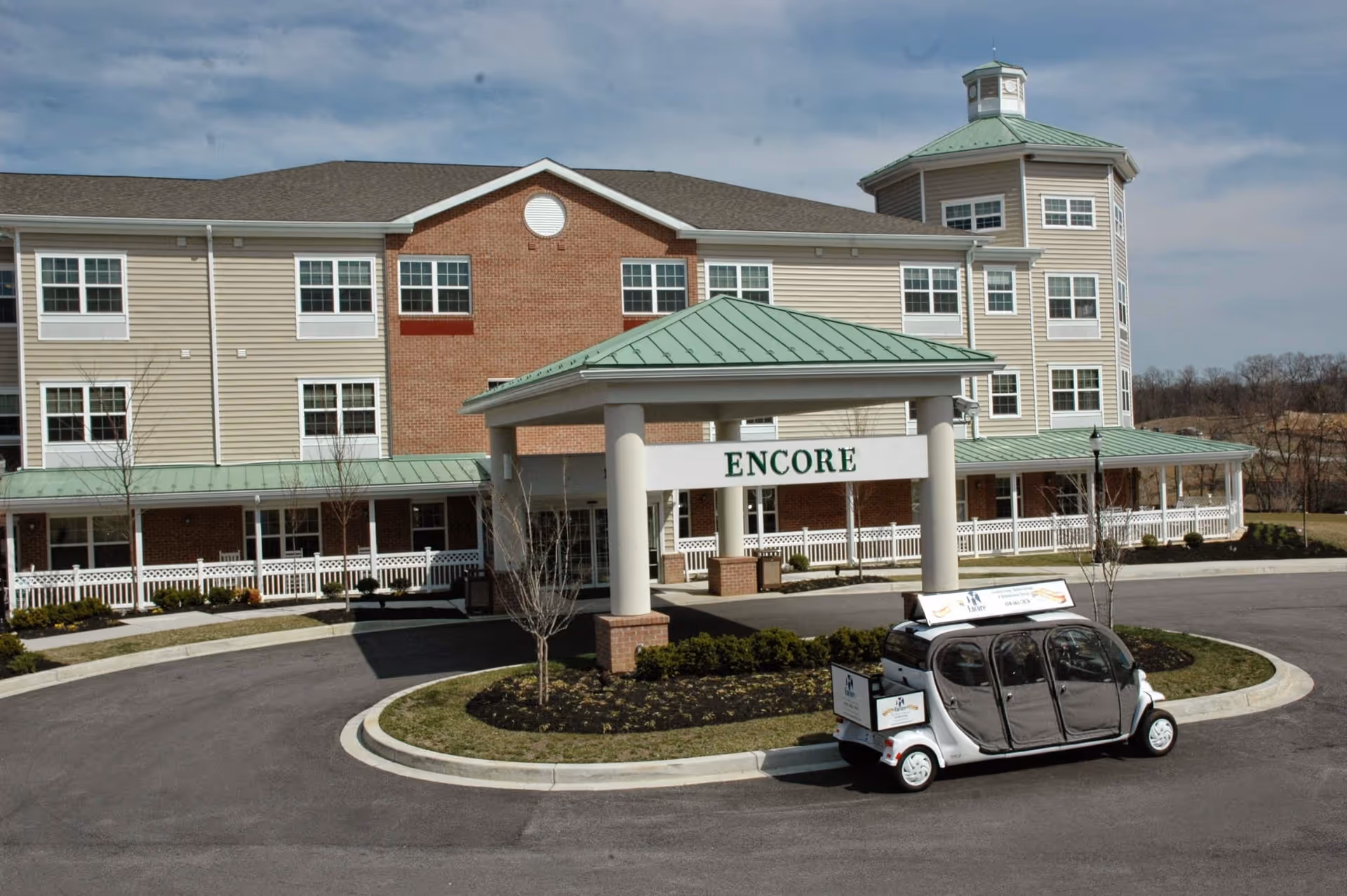 Front entrance of the Lorien Encore senior living building with a covered portico reading 'ENCORE' and a small shuttle vehicle in the circular drive.