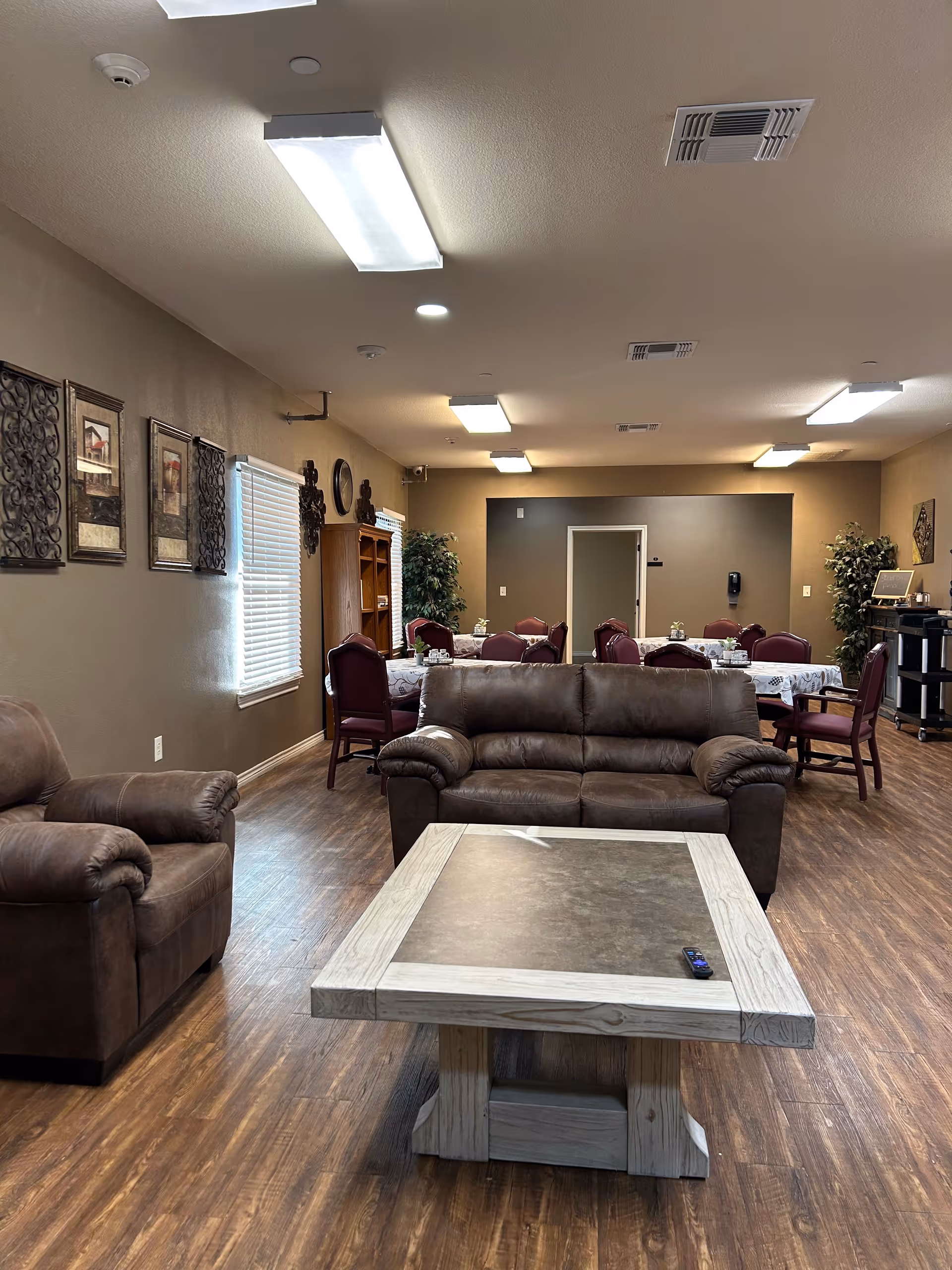 Senior living common area with brown leather sofas, a rectangular coffee table, and dining tables.