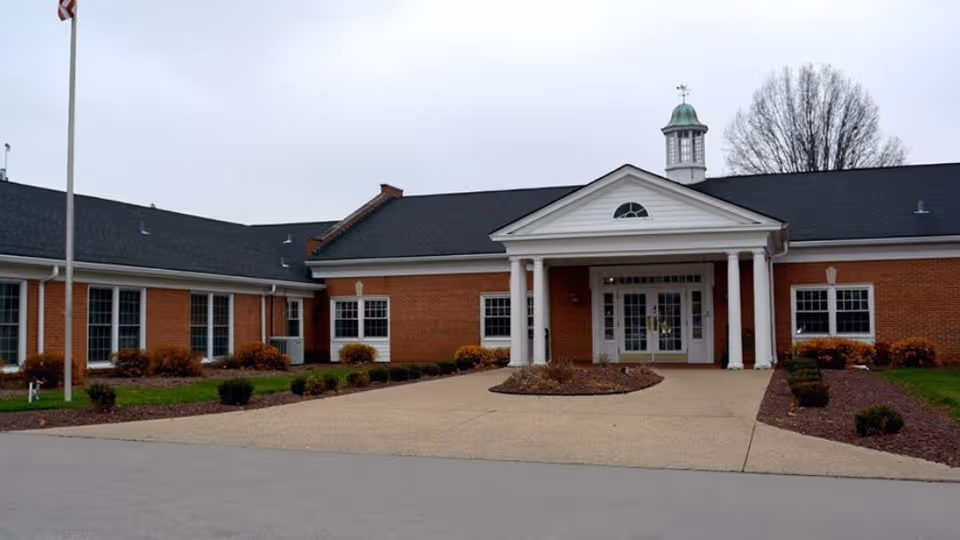 Front view of a brick senior living facility with white columns and circular driveway.