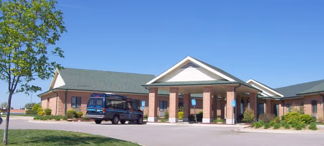 A brick senior living facility front entrance with a covered porte-cochere and a blue van.