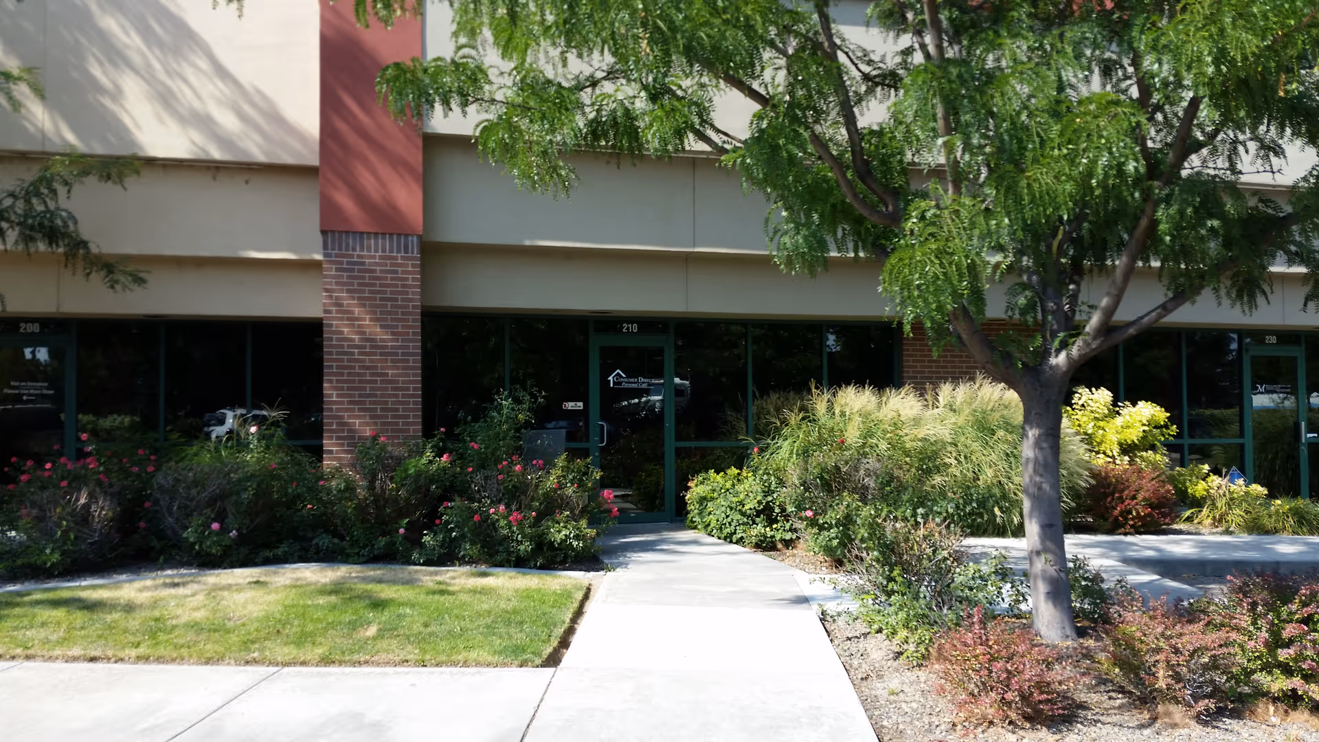 Front of a beige building with glass doors and landscaped shrubs.