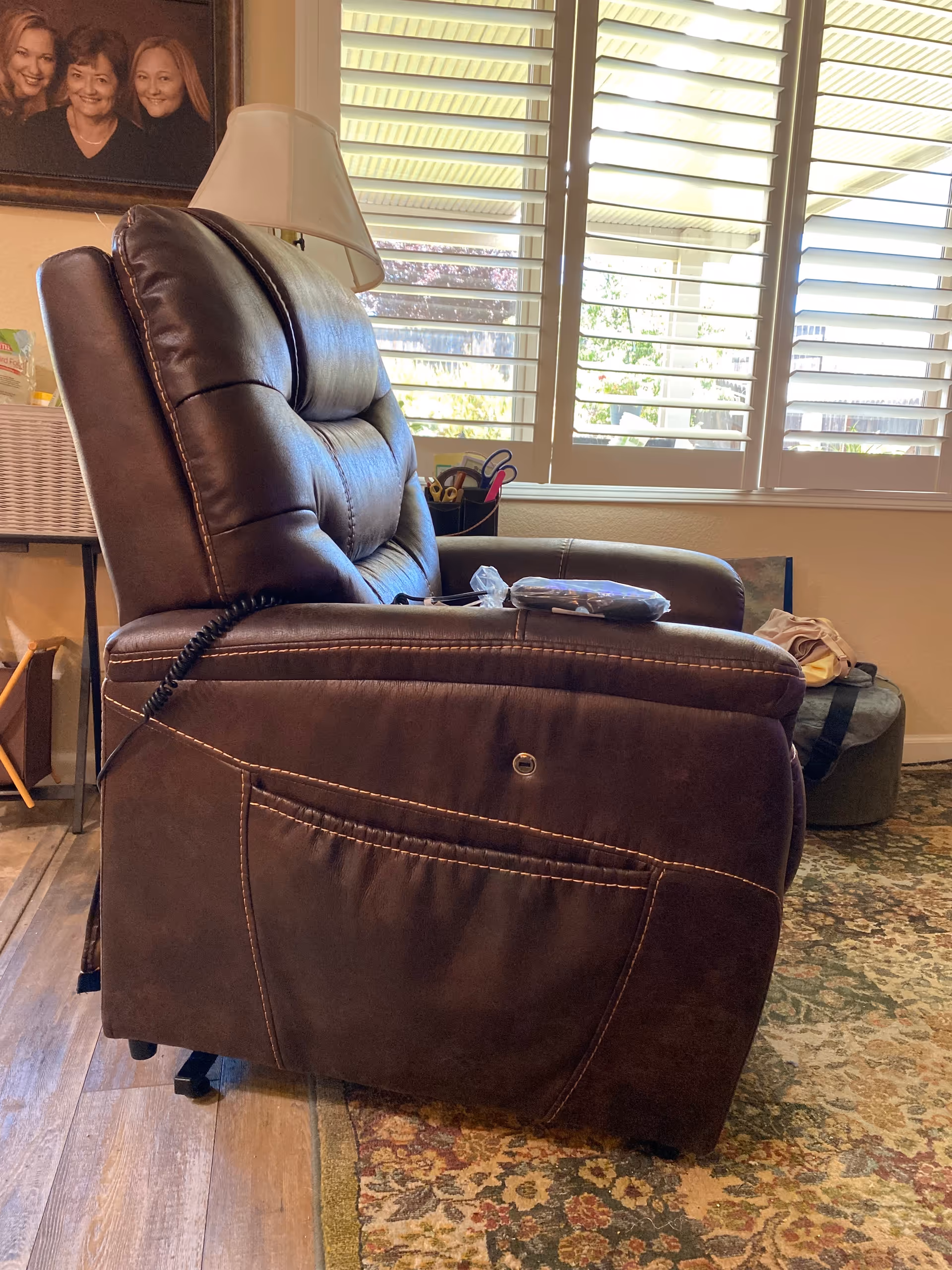 Brown leather recliner chair in a living room with window blinds and a patterned rug.