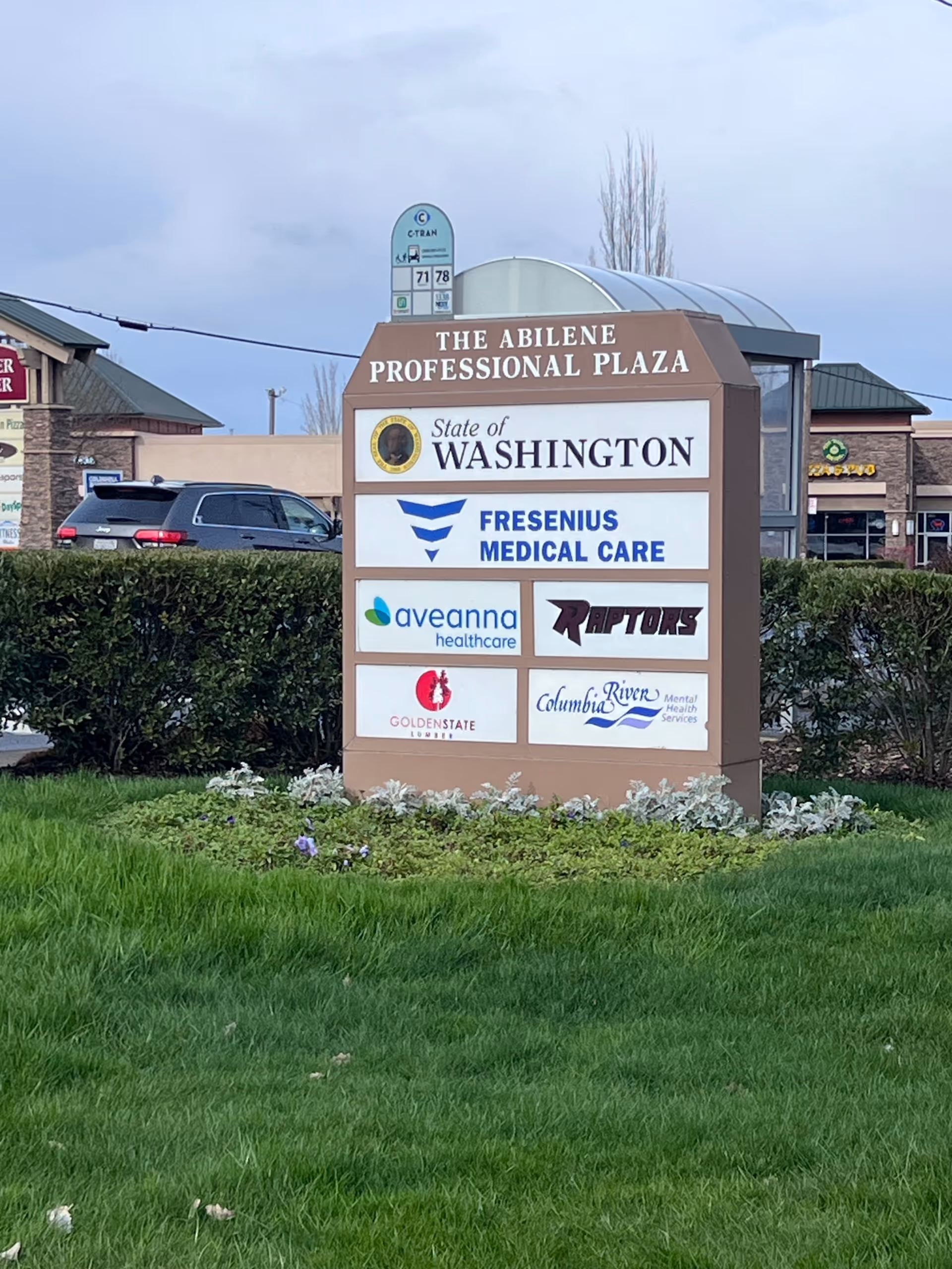 Outdoor sign for The Abilene Professional Plaza with multiple logos and greenery.