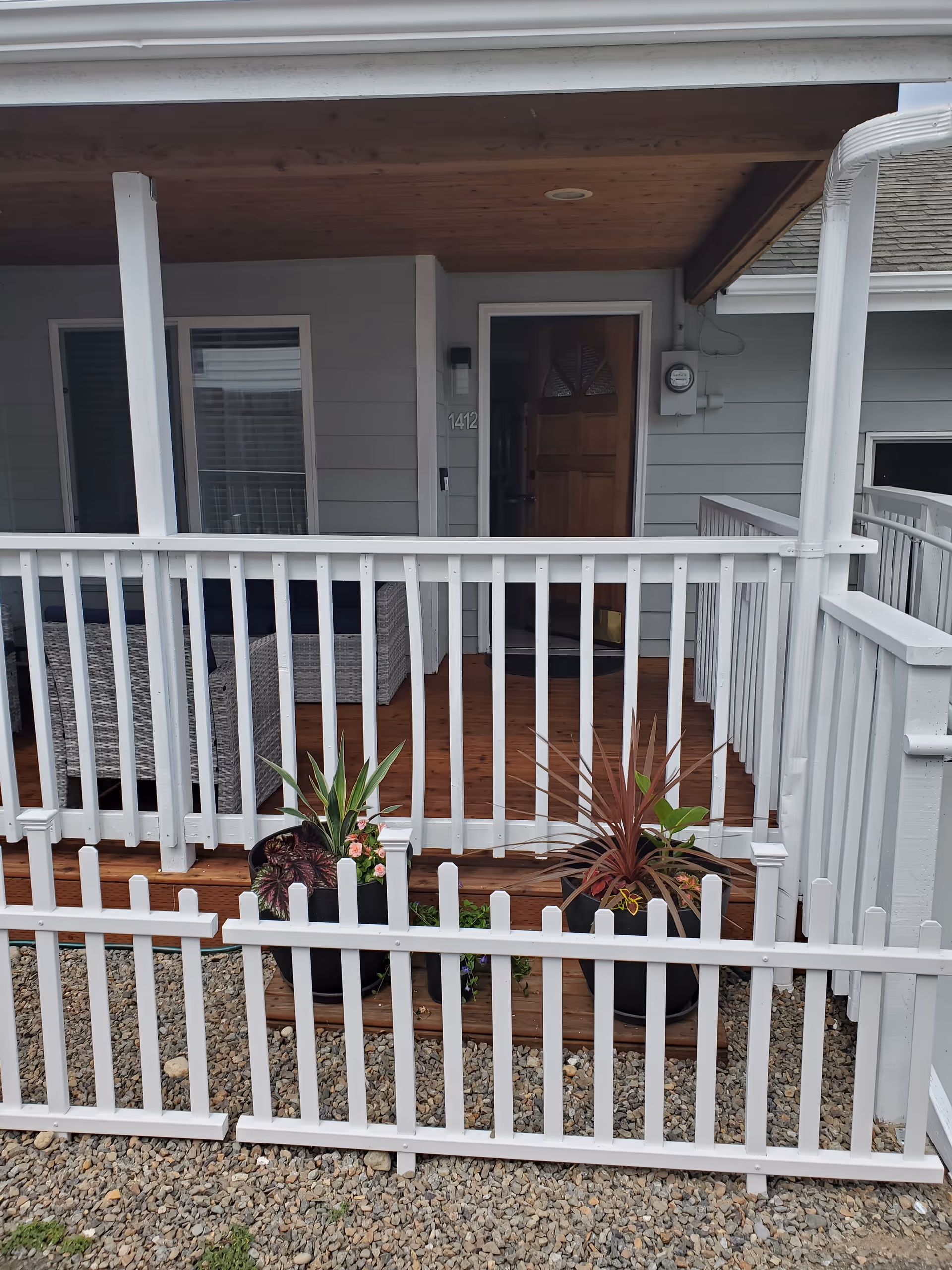 Front porch of a senior living home with white railing, wooden deck, and potted plants.