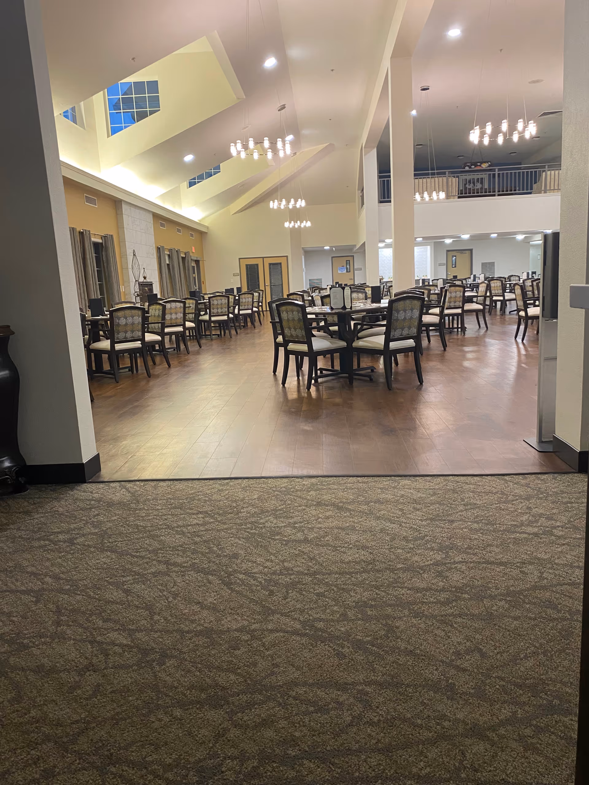 A spacious dining hall with many tables and chairs under bright chandeliers.
