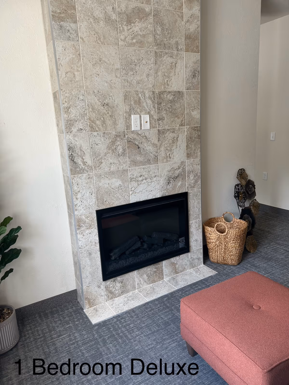 Tile fireplace dominates a cozy living area with a plant, baskets, and a pink ottoman.