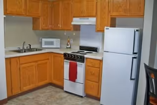 A compact kitchen with wooden cabinets, appliances, and a red towel on the stove.