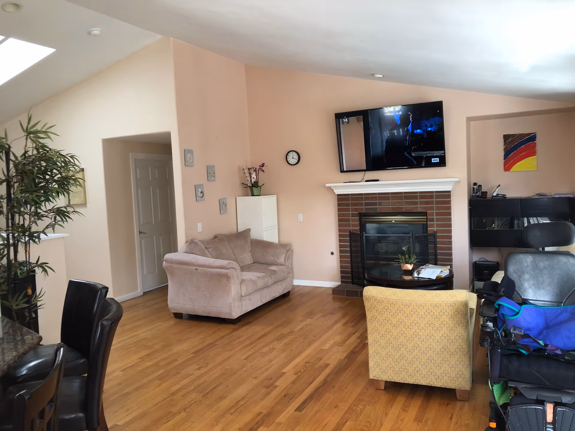 Cozy living room with fireplace, wall-mounted TV, sofa, yellow armchair, and mobility chair.
