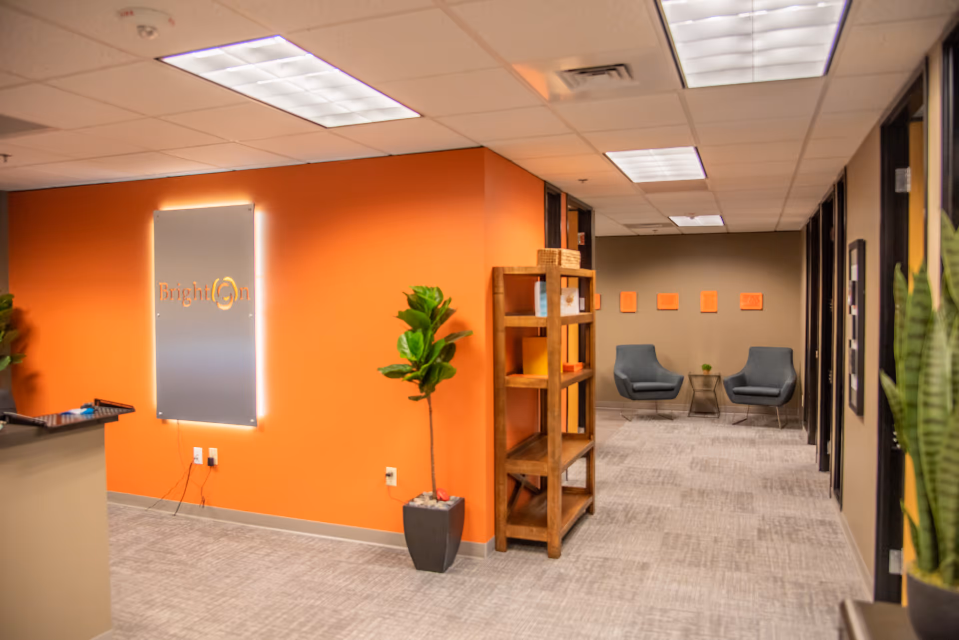 Bright orange-walled lobby with a reception desk, shelves, and two chairs in the back area.