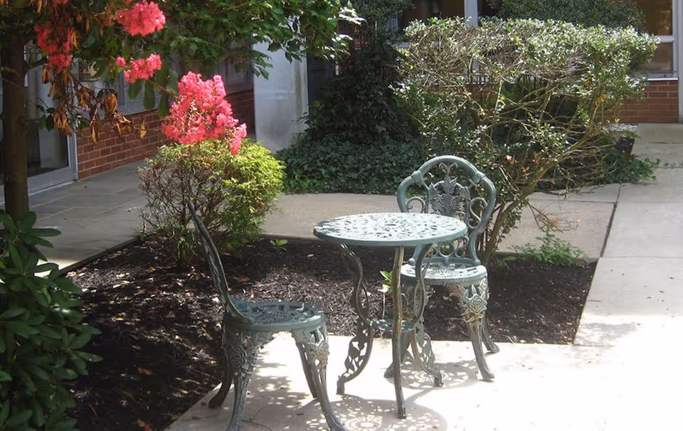 Metal garden table with matching chairs sits in an outdoor courtyard beside a brick building.
