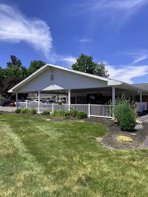 White, single-story senior living facility with a covered front porch and landscaped lawn.