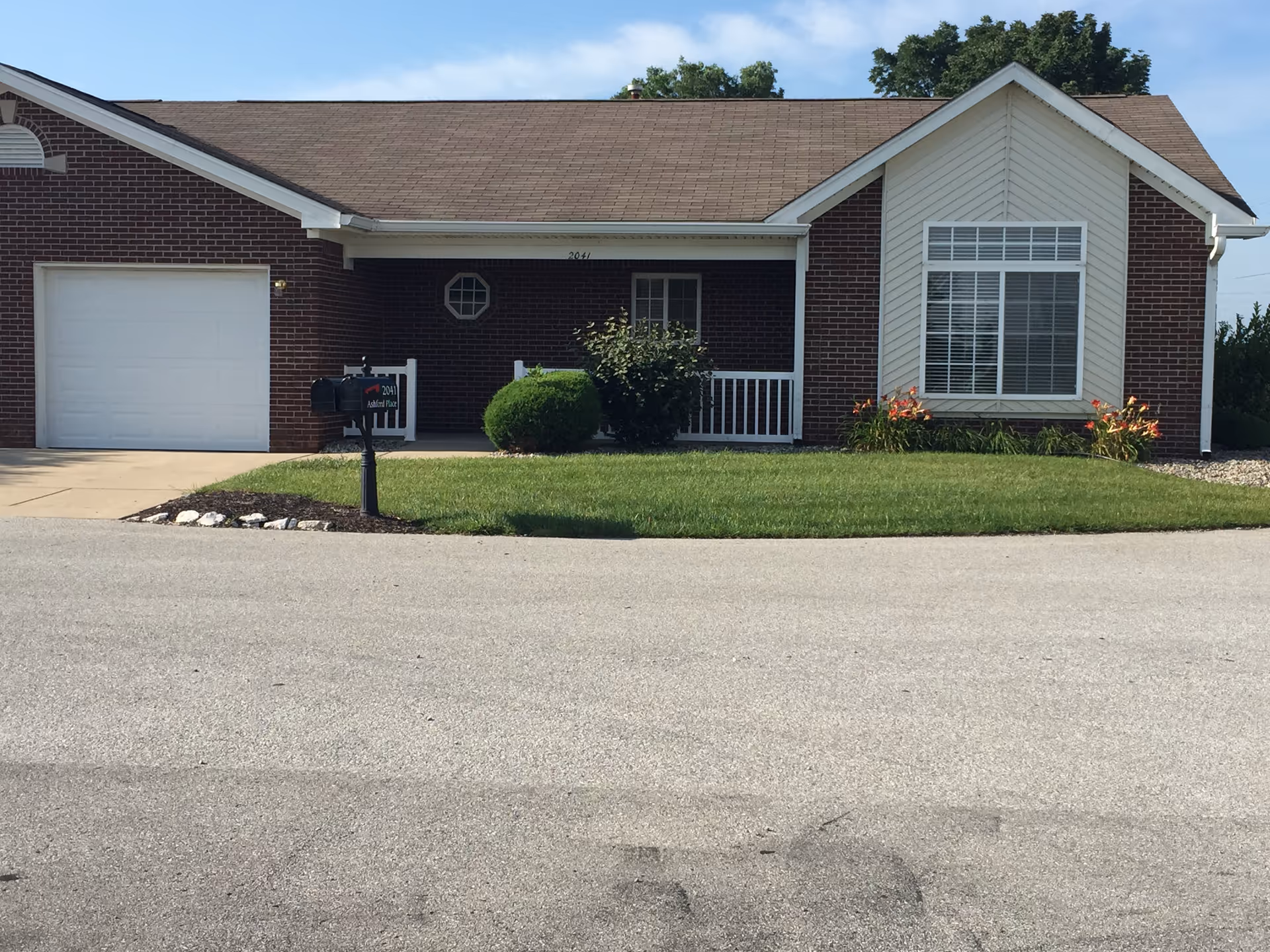 Brick, single-story building with a lawn, driveway, and mailbox in front.