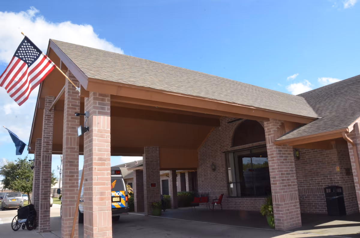 Brick nursing facility entrance with flags, parked ambulance, and a covered drop-off drive.