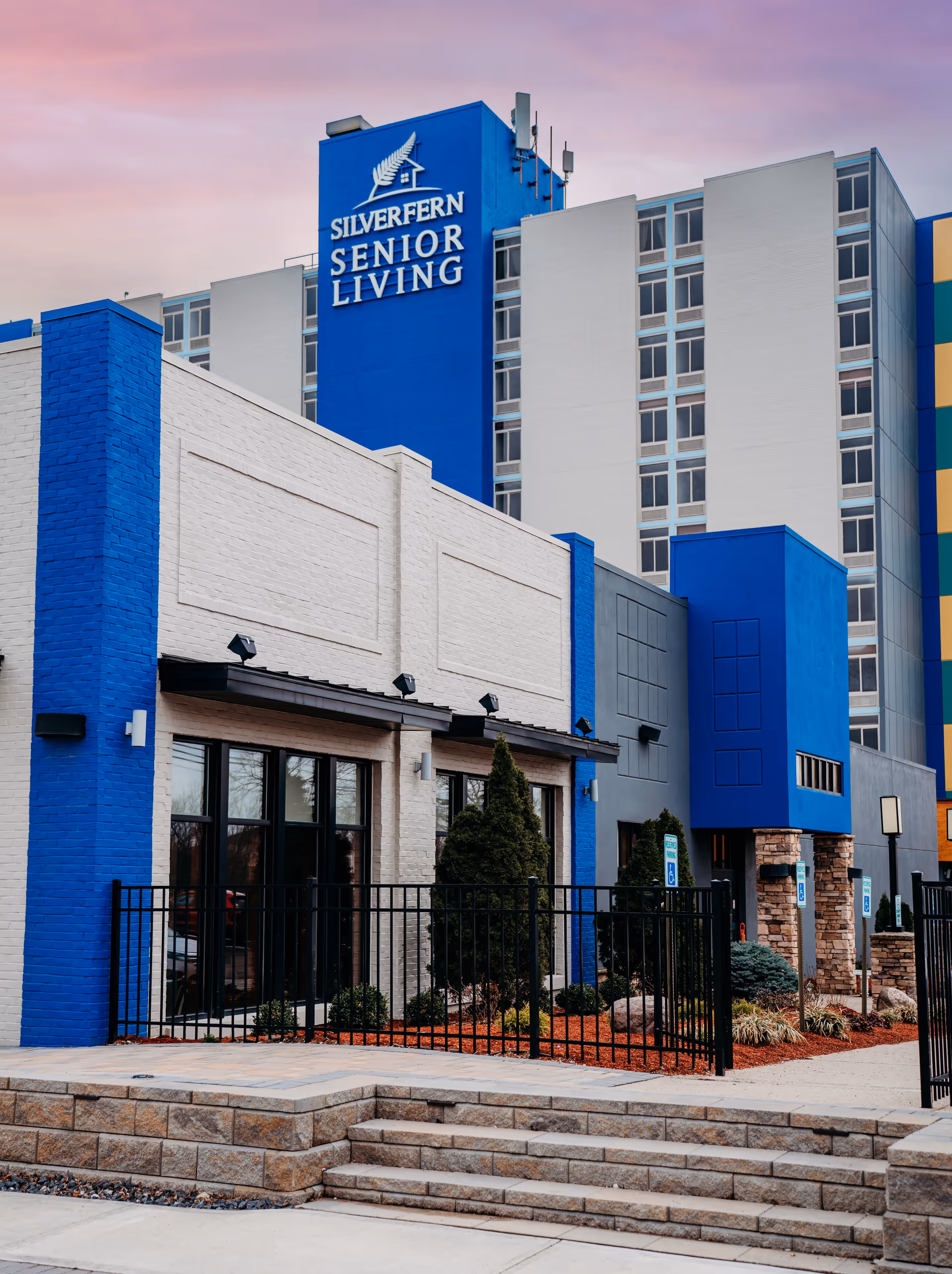 Exterior view of the Silverfern Senior Living building showing a blue-and-white facade with signage and entrance steps.