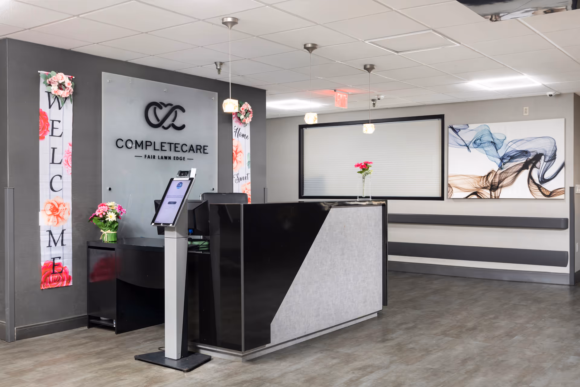Reception desk in a modern lobby with wall art and floral decorations.