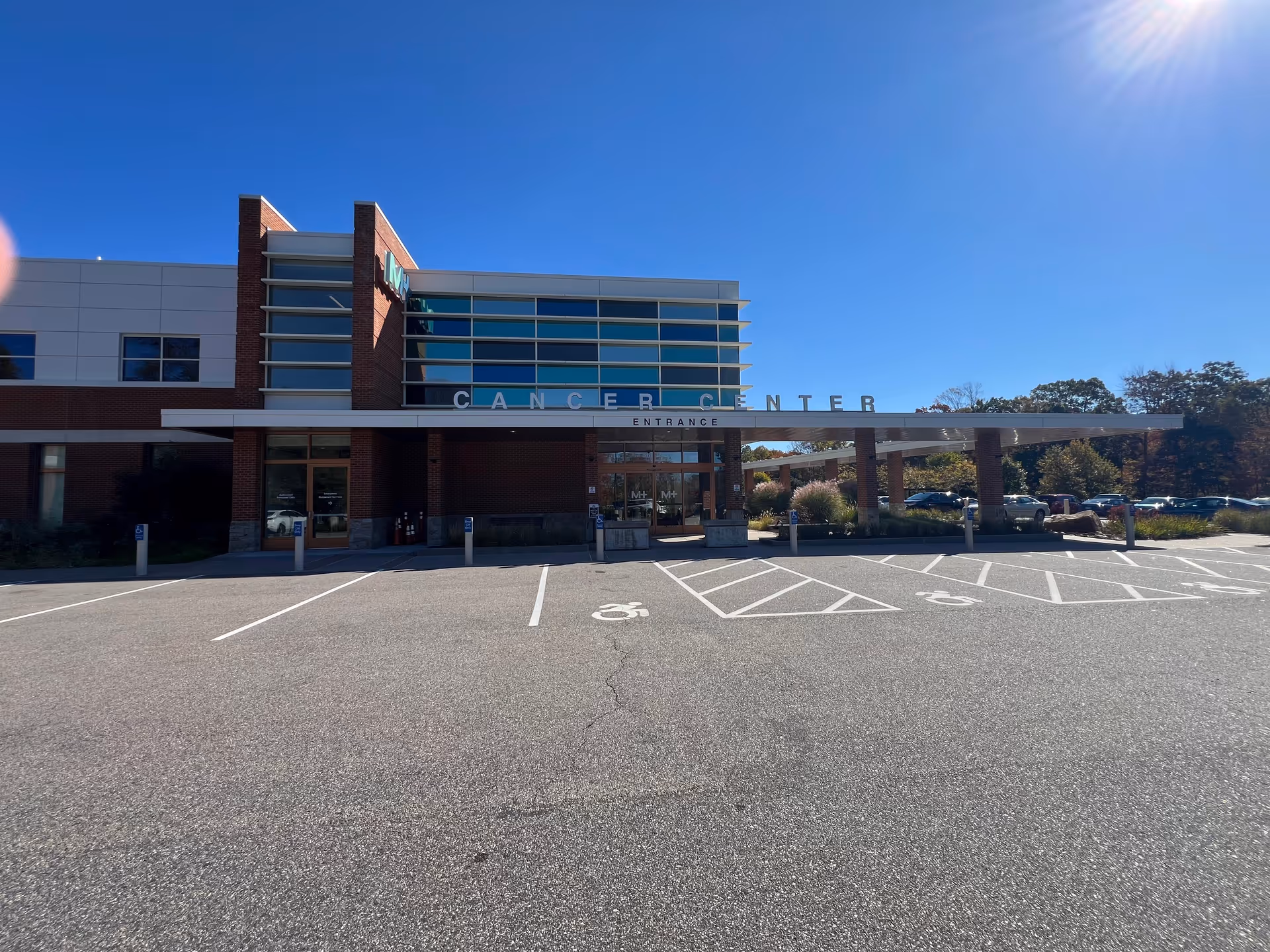 Cancer Center entrance of a modern medical building with parking lot and blue sky.