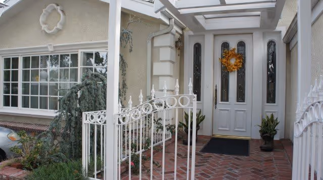White entrance with wreath, glass doors, brick porch, ornamental railing, and a parked car.