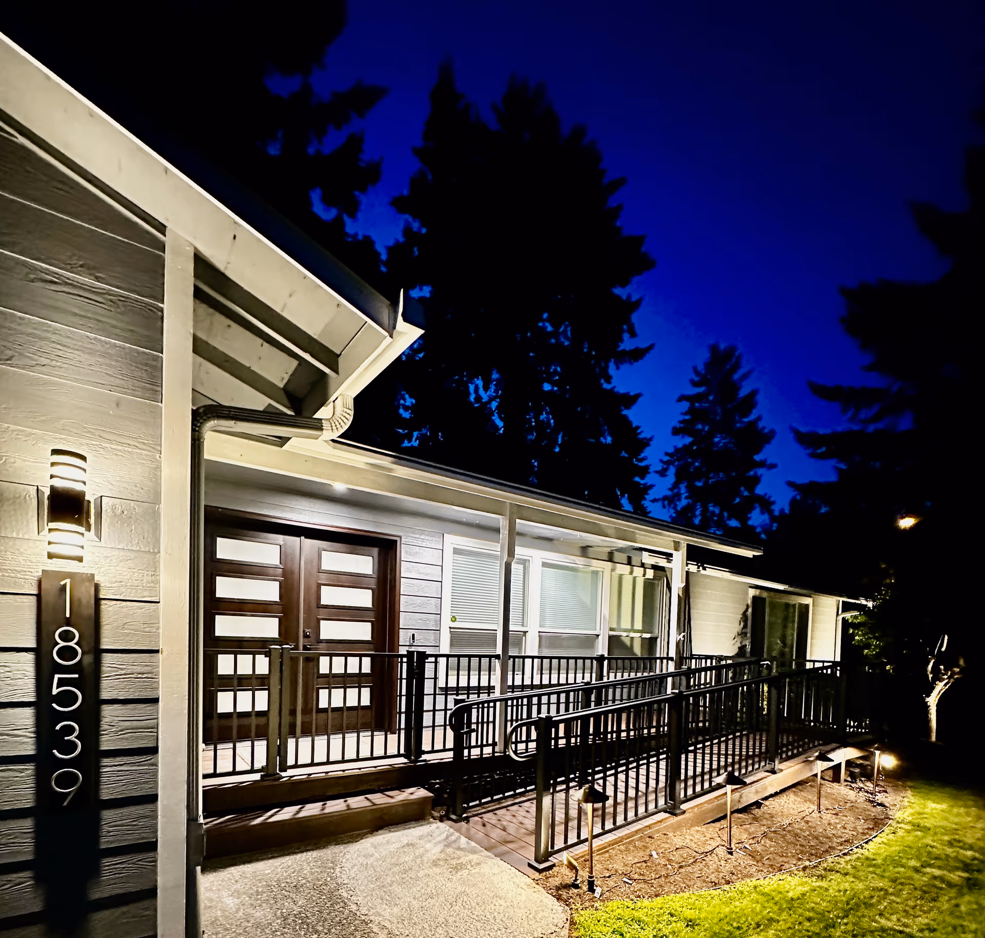 Night exterior of a single-story facility with a front entrance, ramp, and address plaque.