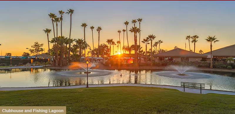 Sunset over a lagoon with fountains, palm trees, and clubhouse buildings.