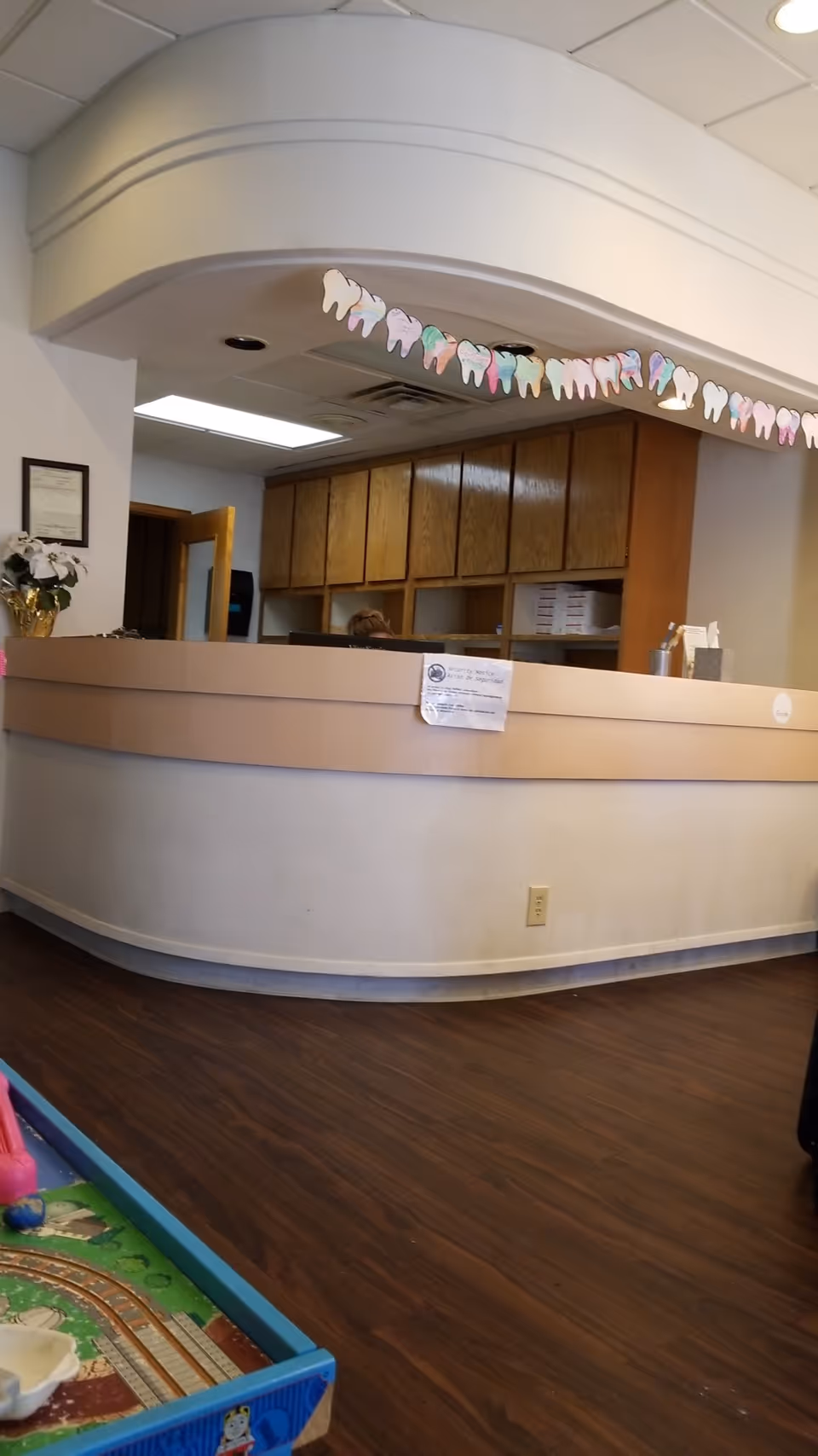 Curved reception desk in a lobby with wooden cabinets and a children's play area.