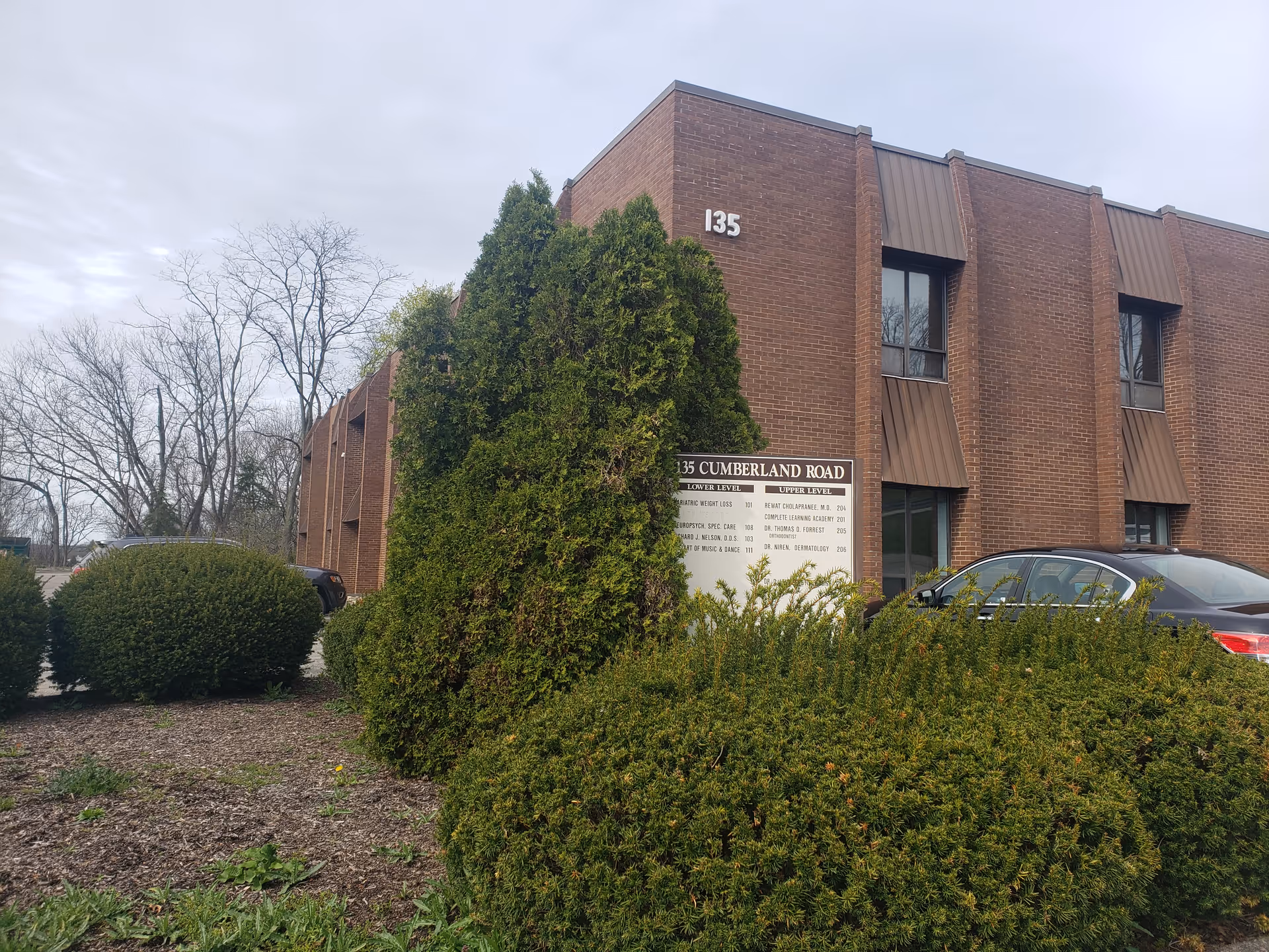 Brick exterior of a senior care facility with a sign and shrubs.