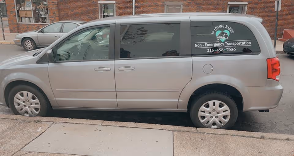 Silver minivan with In Loving Hands logo advertising Non-Emergency Transportation on street.