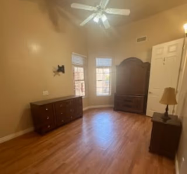 An empty bedroom showing a dresser, armoire, lamp, and ceiling fan.