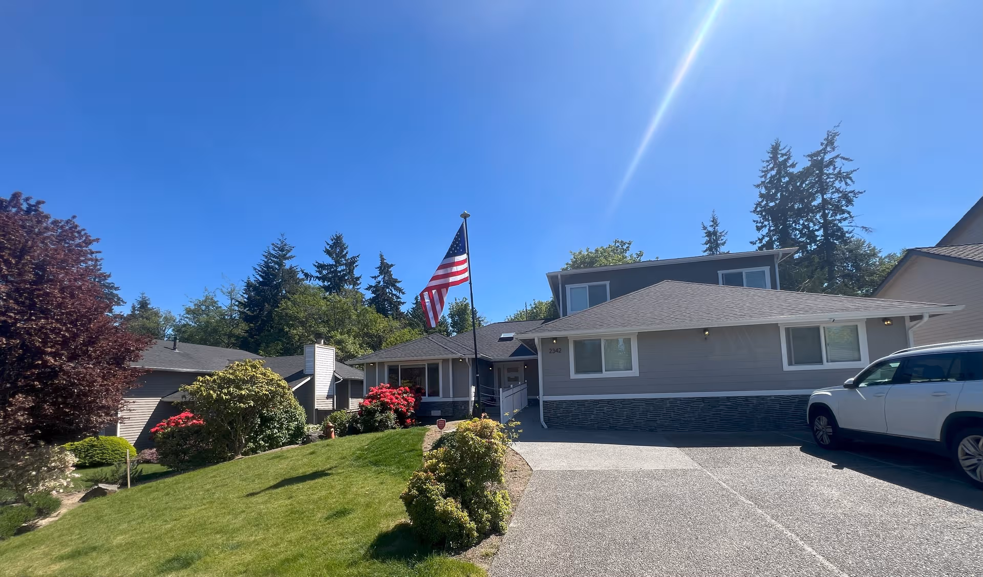 Single-story senior care facility exterior with an American flag on a flagpole, manicured lawn, and driveway.