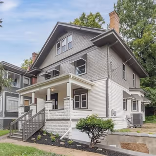 Two-story gray and white senior living house with a covered front porch and stairs.