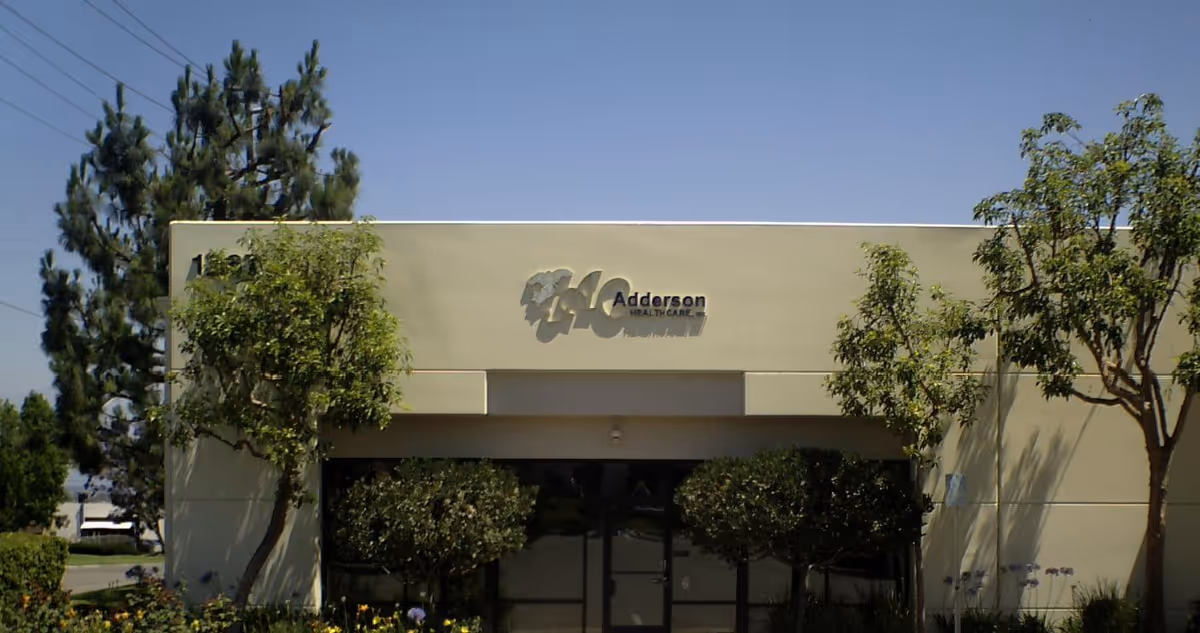 Exterior of a beige healthcare building with logo and trees.