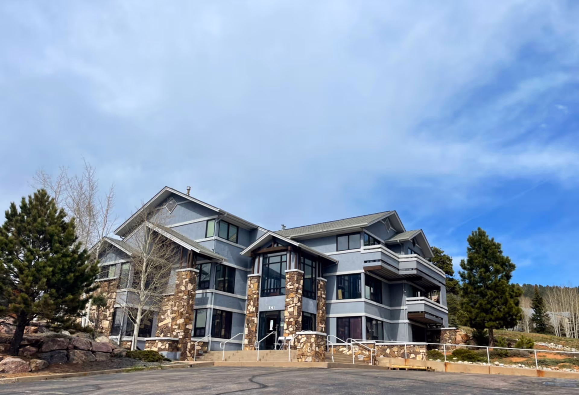 Multi-story modern senior living building with stone pillars, glass entrances, and balconies under a blue sky.