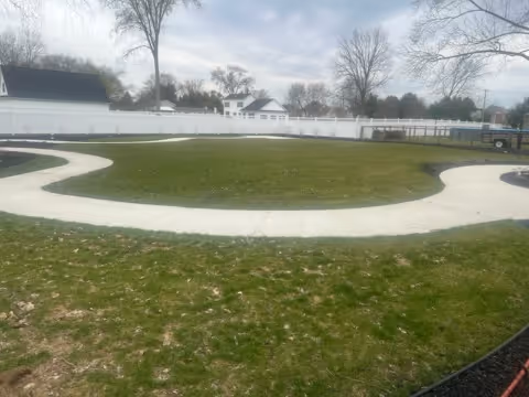 A circular courtyard with green lawn, curved white walkway, and white fencing.