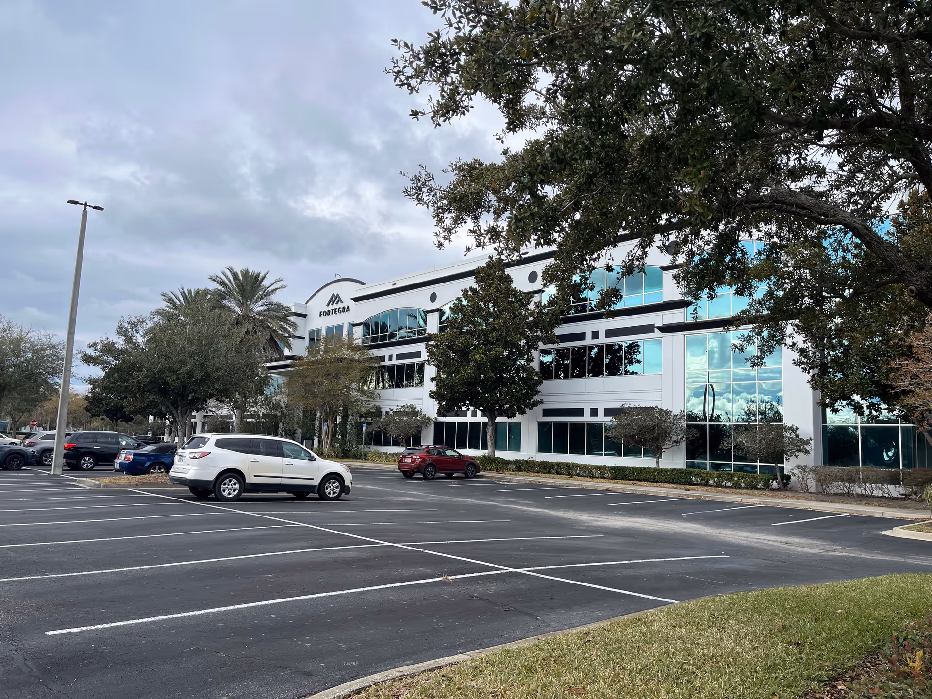 Exterior view of a modern multi-story medical facility with glass windows and surrounding parking lot.