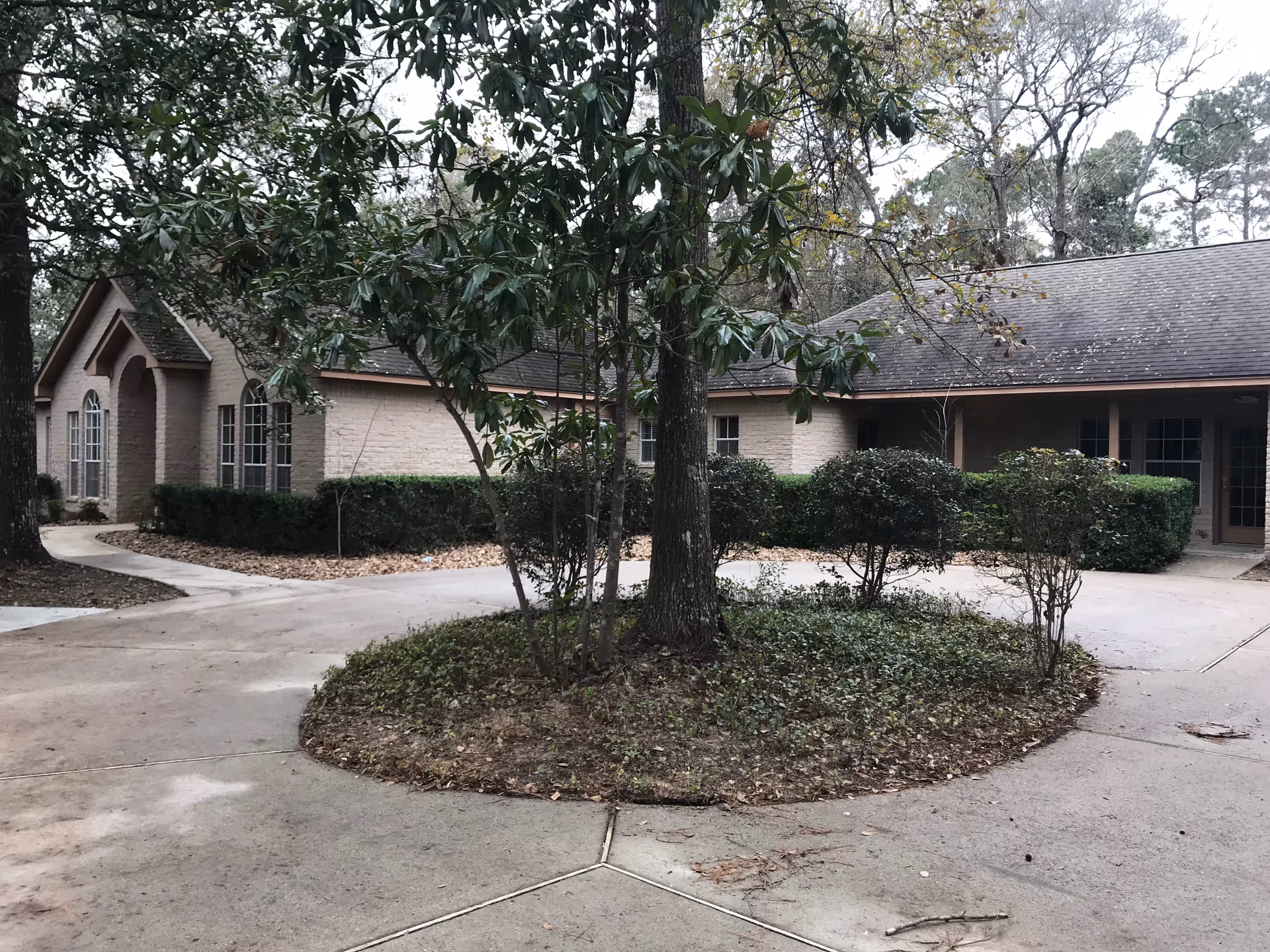 Circular driveway and front courtyard with trees and hedges in front of a single-story brick building.