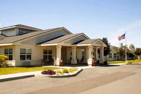 Single-story senior living center with a covered entrance, flagpole, and manicured landscaping.