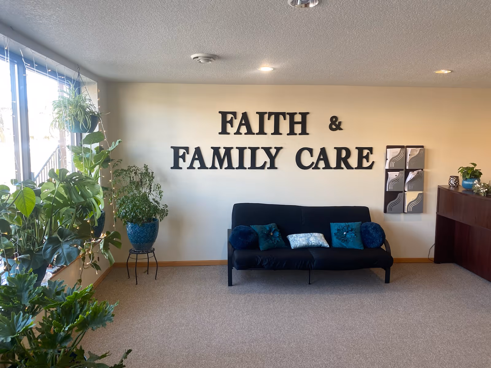 Lounge area with a black sofa, plants, and a Faith & Family Care sign.