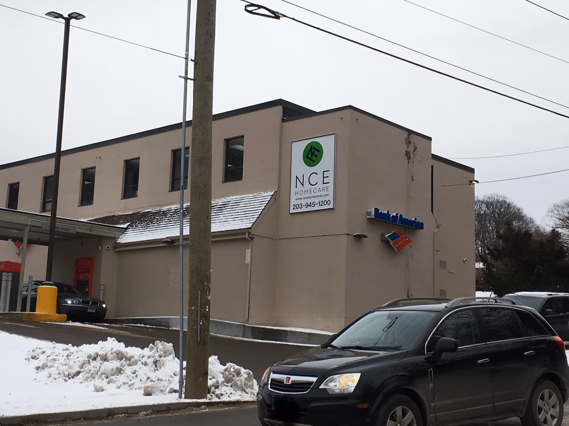 Exterior view of a beige building with NCE Homecare sign, parked cars, and snow.