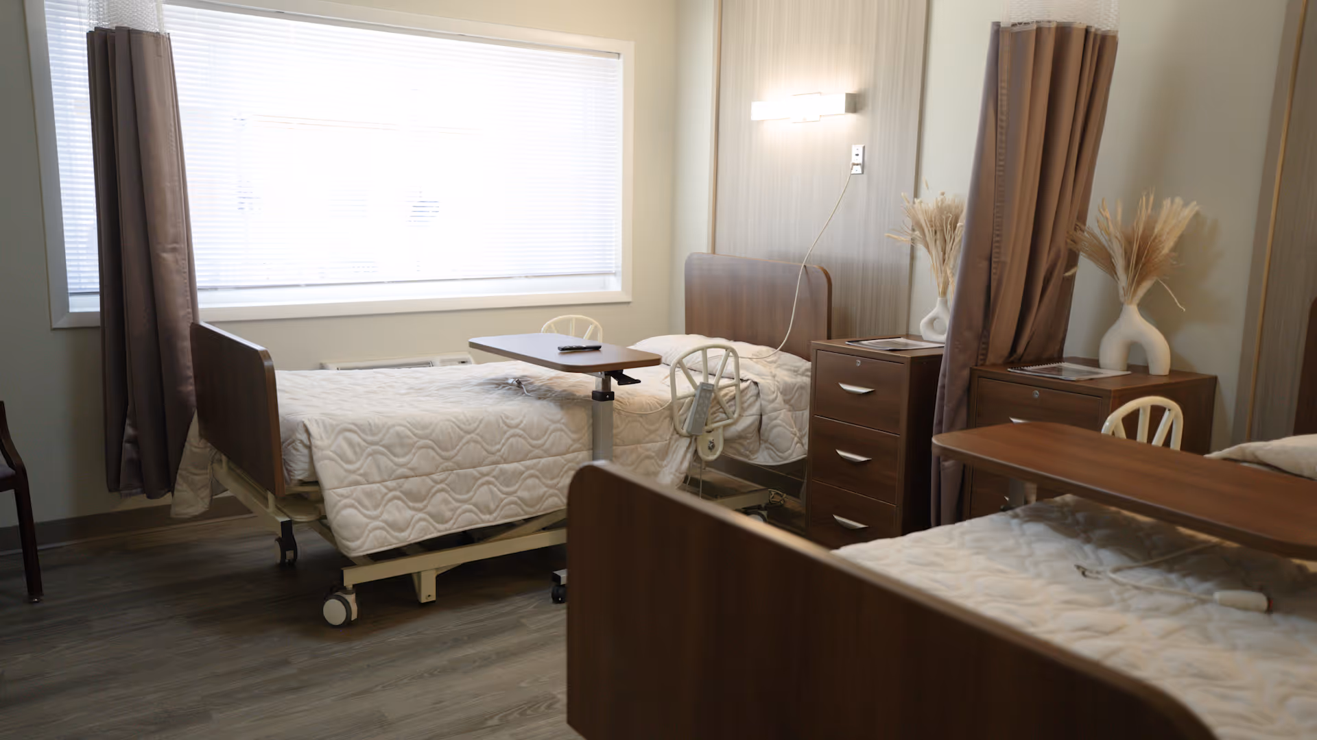 Shared senior living bedroom with two beds, privacy curtains, and wooden furniture.